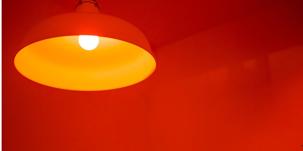 Contemporary red pendant ceiling lamp with warm yellow glow, minimalist lighting fixture for modern interiors, industrial-style decor, ambient illumination, and creative home or café design aesthetics.
